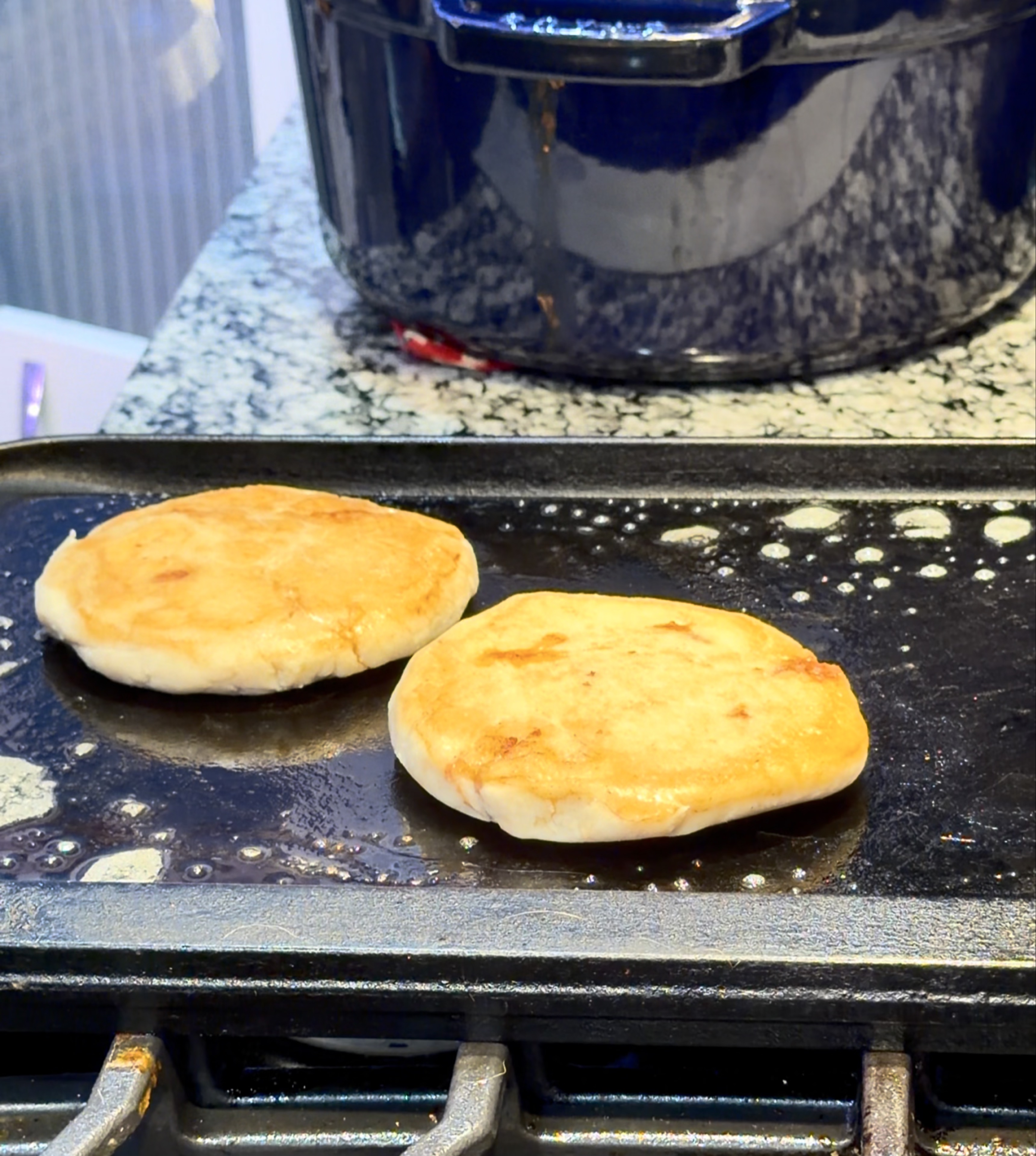 Two pupusas browning on a flat griddle